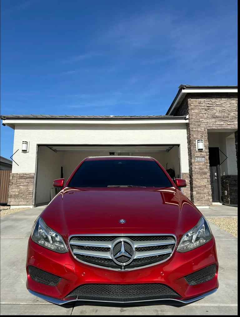 Red Mercedes-Benz sedan parked in driveway in front of open garage door on clear sunny day